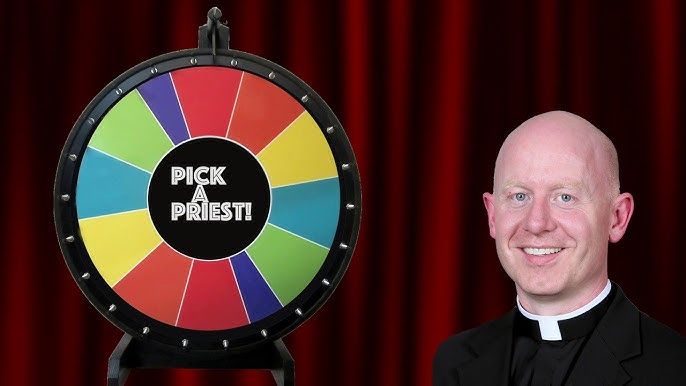 A spinning prize wheel is set up beside a person. The prize-wheel has the words "Pick a Priest!" in the center. The person is smilling, has light skin, is bald and is wearing a style of neckband common to Christian clergy members.